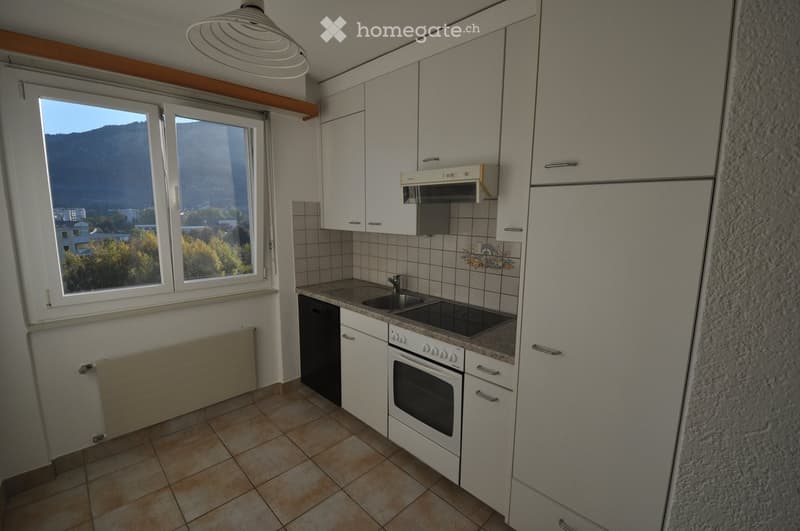Modern kitchen with white cabinets, stainless steel appliances, and a view of mountains through large windows.