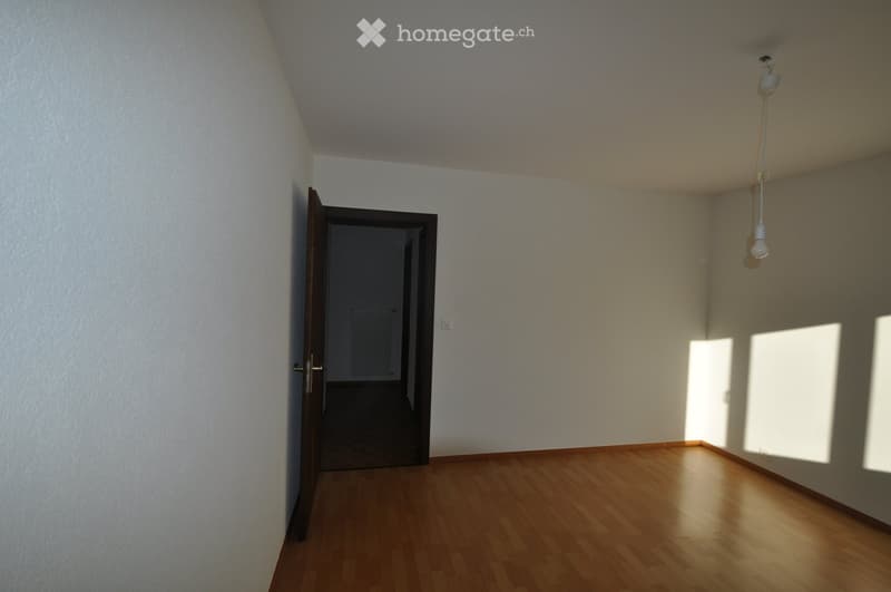 Empty room with wooden flooring, white walls, and a single open door leading to another space. Natural light streams in from the right side.