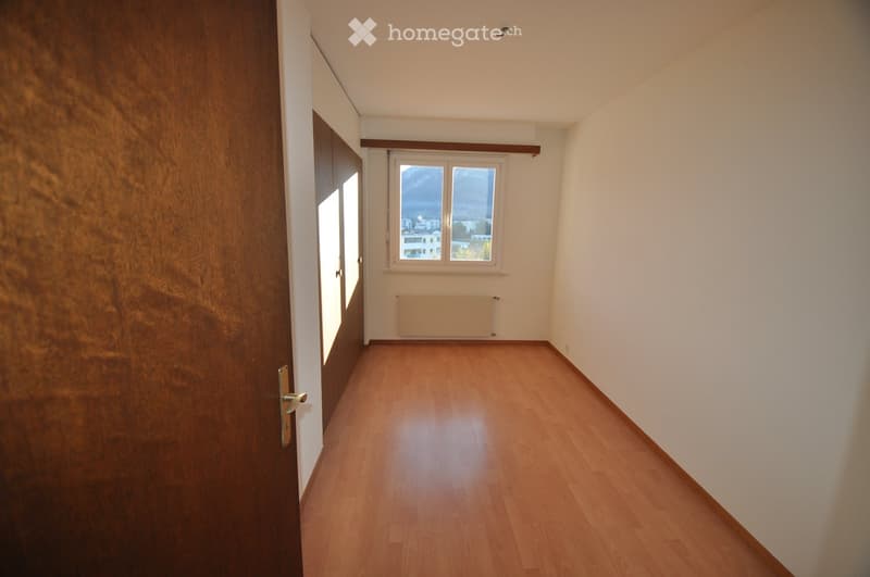 Empty room with wooden flooring, white walls, a window with a view, and a radiator. No furniture or equipment is present.