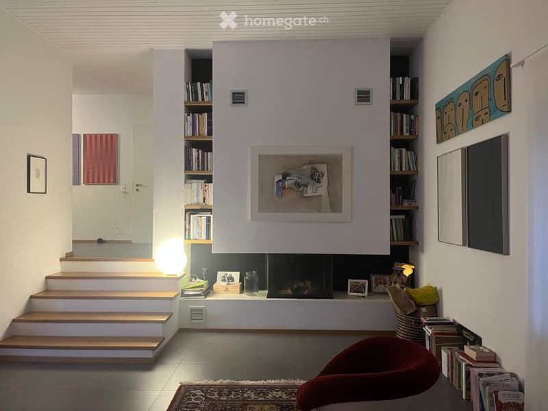 Modern living room with a fireplace, bookshelf, sofa, and artwork on the walls.