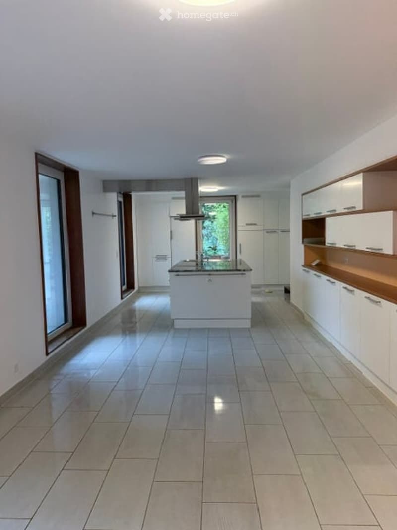 Modern kitchen with white cabinets, a central island, and a range hood. The space features large windows and tiled flooring.