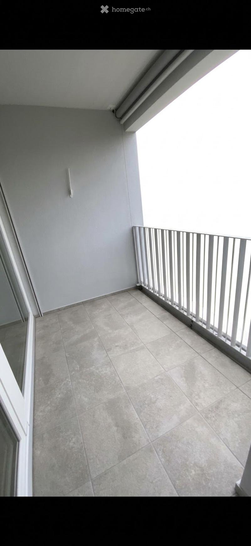 Empty balcony with tiled floor and white metal railing, featuring a light fixture on the wall.