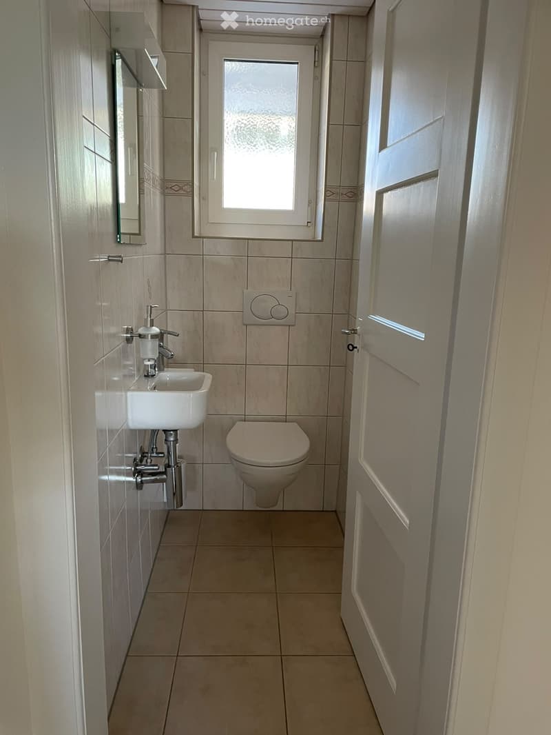 Small bathroom with beige tiles, a white sink, a toilet, and a mirror on the wall.