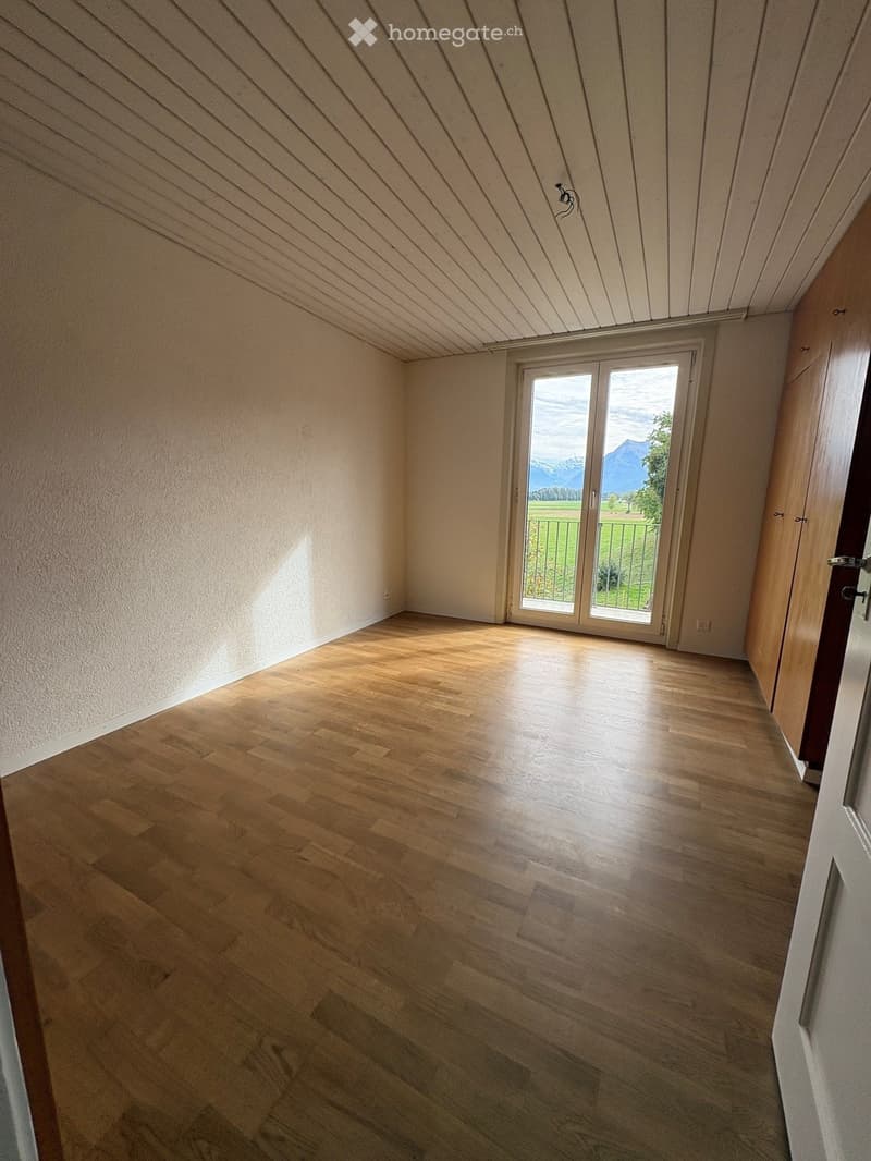 Empty room with wooden flooring, white walls, and a large sliding glass door leading to a balcony with a scenic mountain view.