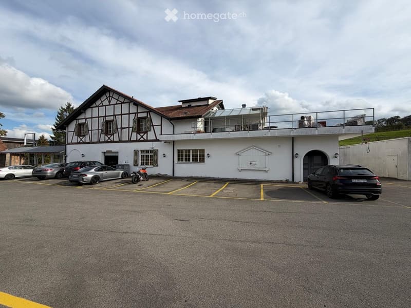 Two-story building with a balcony, parking area with several cars, and a motorcycle.