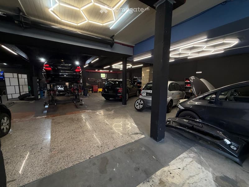 Garage with multiple cars, some on lifts, and tools and equipment visible in the background.