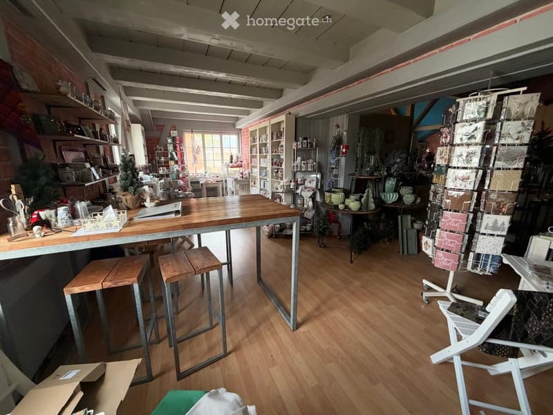 A well-lit, rustic-style shop interior with wooden flooring, a large central table, shelves filled with various items, and a display of cards and gifts.