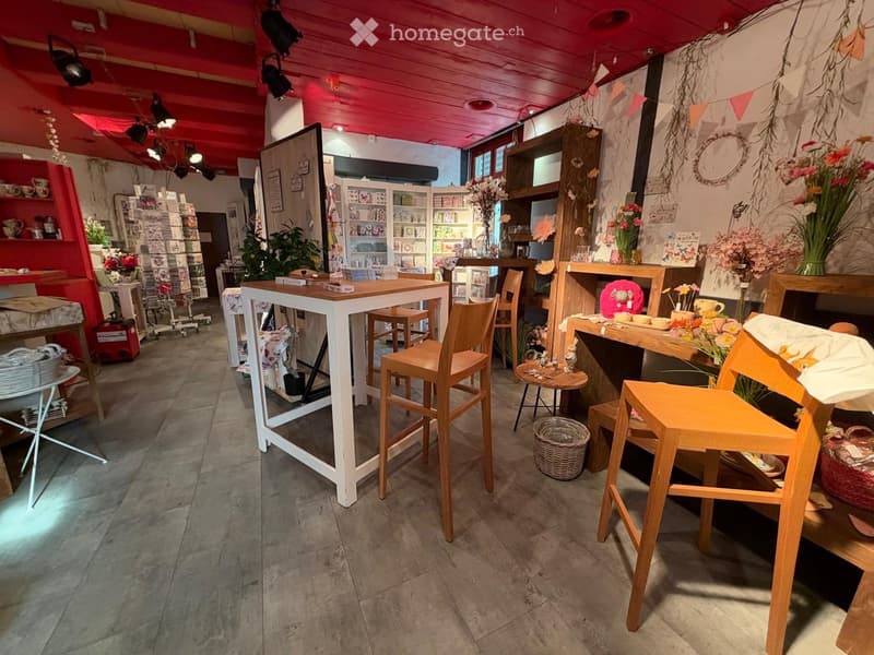 A cozy, well-decorated shop interior with wooden tables, chairs, shelves filled with items, and decorative vases.
