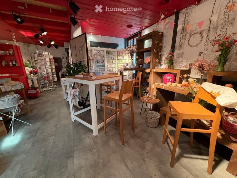 A cozy, well-lit shop interior with wooden tables, chairs, shelves filled with items, and decorative vases.