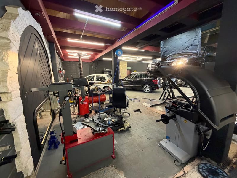 A well-lit garage with multiple cars, a hydraulic lift, a tire machine, and various tools and equipment.