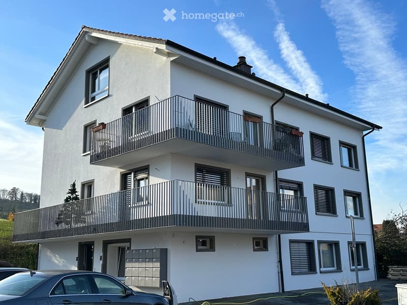 Modern two-story apartment building with white exterior, multiple balconies, and a parking area.