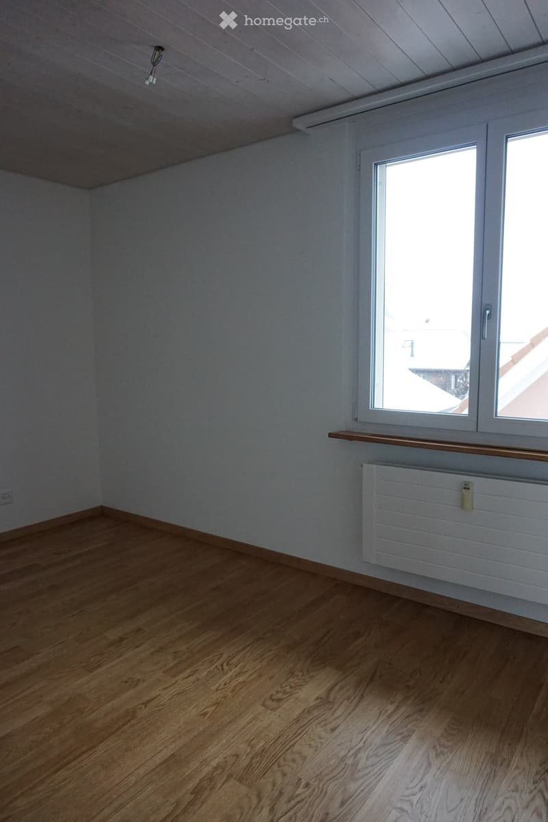 Empty room with wooden flooring, white walls, and a window with a wooden sill. A radiator is visible below the window.