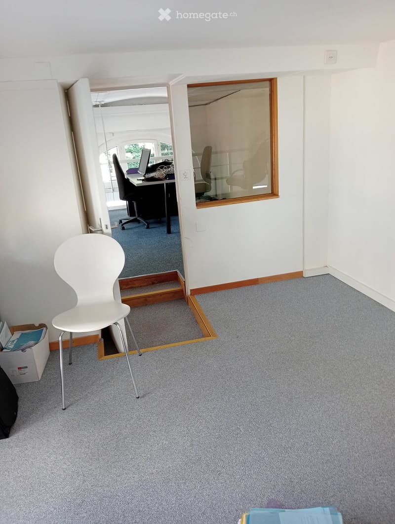 A furnished room with a white chair, a desk with a computer, and an office chair visible through an open doorway.