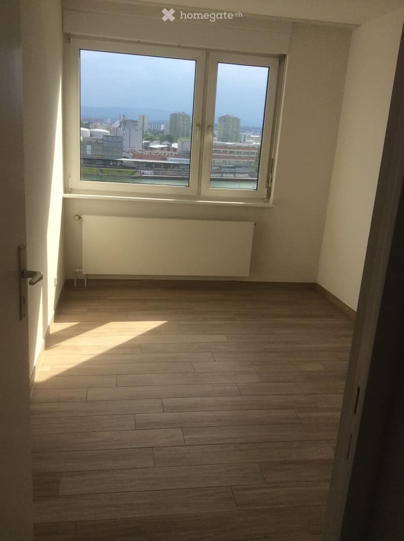 Empty room with wooden flooring, large windows offering a city view, and a radiator below the windows.