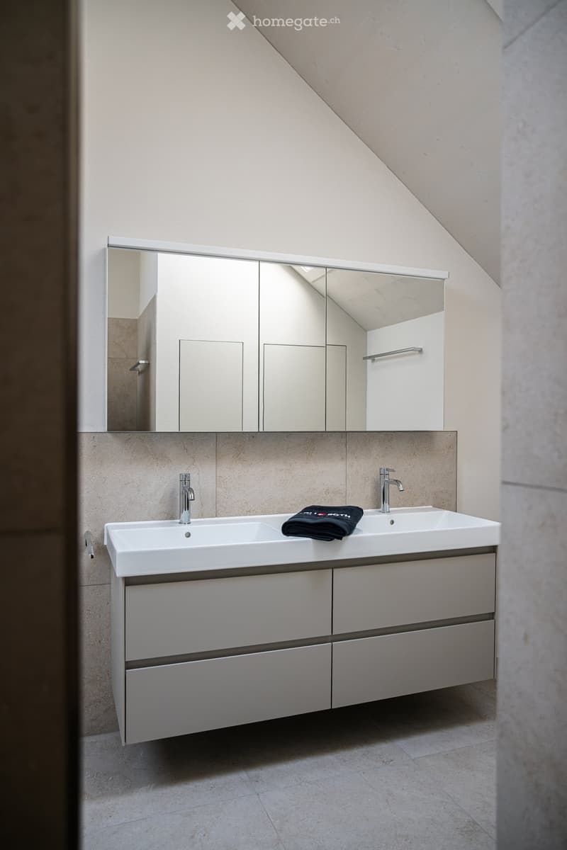 Modern bathroom with a double sink, sleek mirrored cabinet, and a folded black towel on the counter.