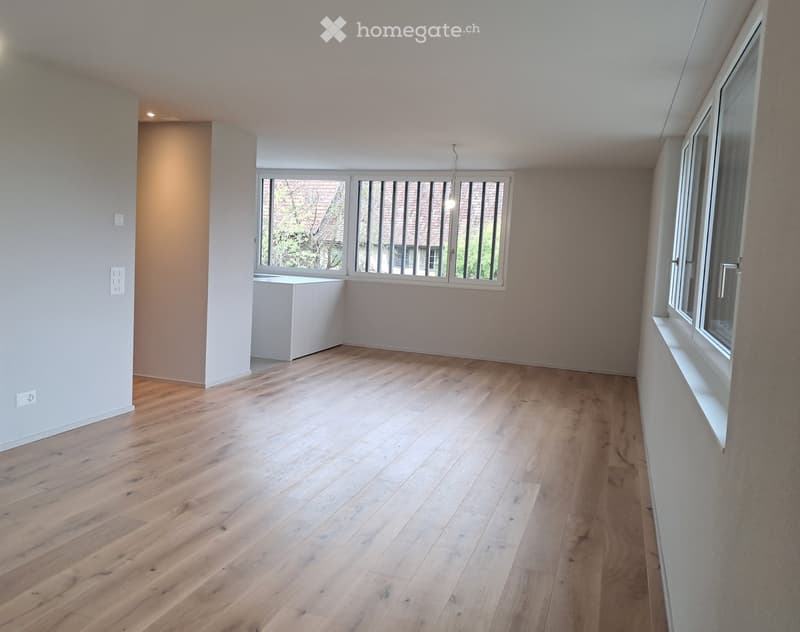 Empty room with light wooden flooring, white walls, and large windows with blinds. No furniture or equipment present.