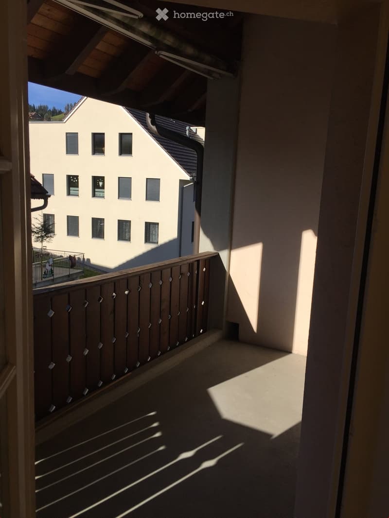 Balcony with wooden railing, overlooking a building with multiple windows and a small garden area.