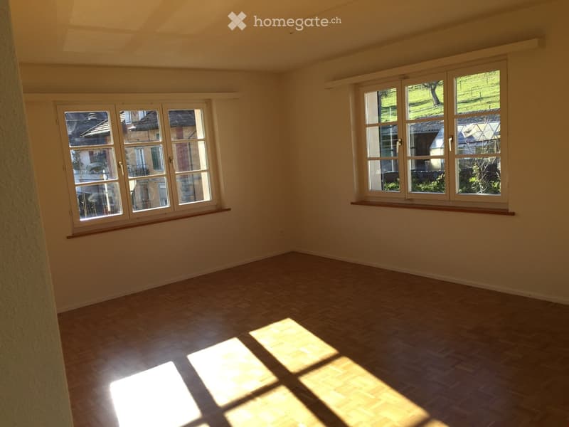 Empty room with wooden flooring and large windows, allowing natural light to fill the space.