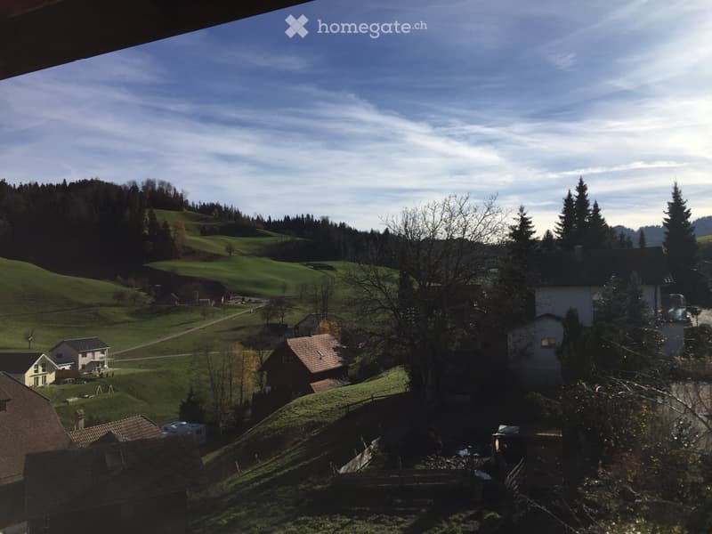 A scenic view of a rural village with houses, green hills, and trees under a partly cloudy sky.