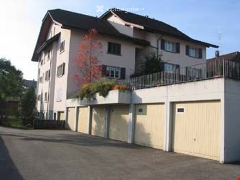 Multi-story residential building with a flat roof, multiple windows, and a row of attached garages.