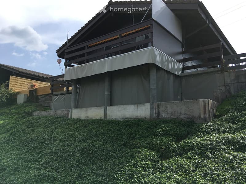 Two-story house with a raised ground floor, balcony, and covered outdoor area. The structure features a modern design with a concrete base and wooden elements.