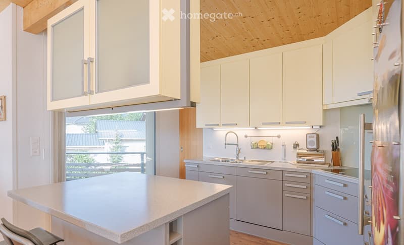 Modern kitchen with light-colored cabinets, a central island, and stainless steel appliances. Features include a sink with a modern faucet, a refrigerator, and a toaster on the counter.