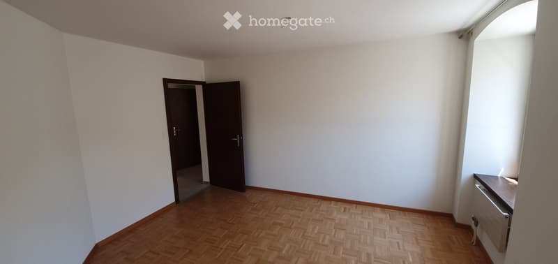 Empty room with wooden flooring, white walls, and a single door leading to another space. No furniture or equipment is present.