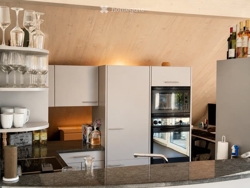 Modern kitchen with white cabinets, stainless steel appliances, and wooden accents. Features include a built-in oven, a sink with a modern faucet, and open shelving displaying wine glasses and cups.