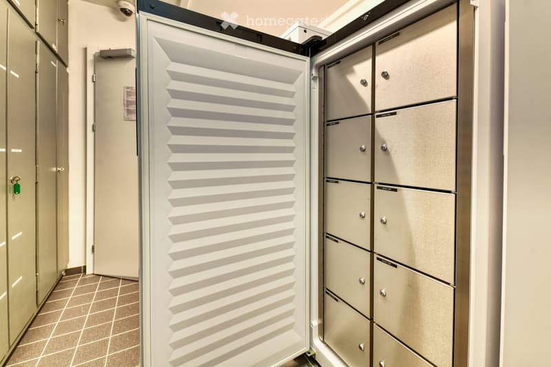 A hallway with a security camera, a door, and a row of lockers with silver handles.
