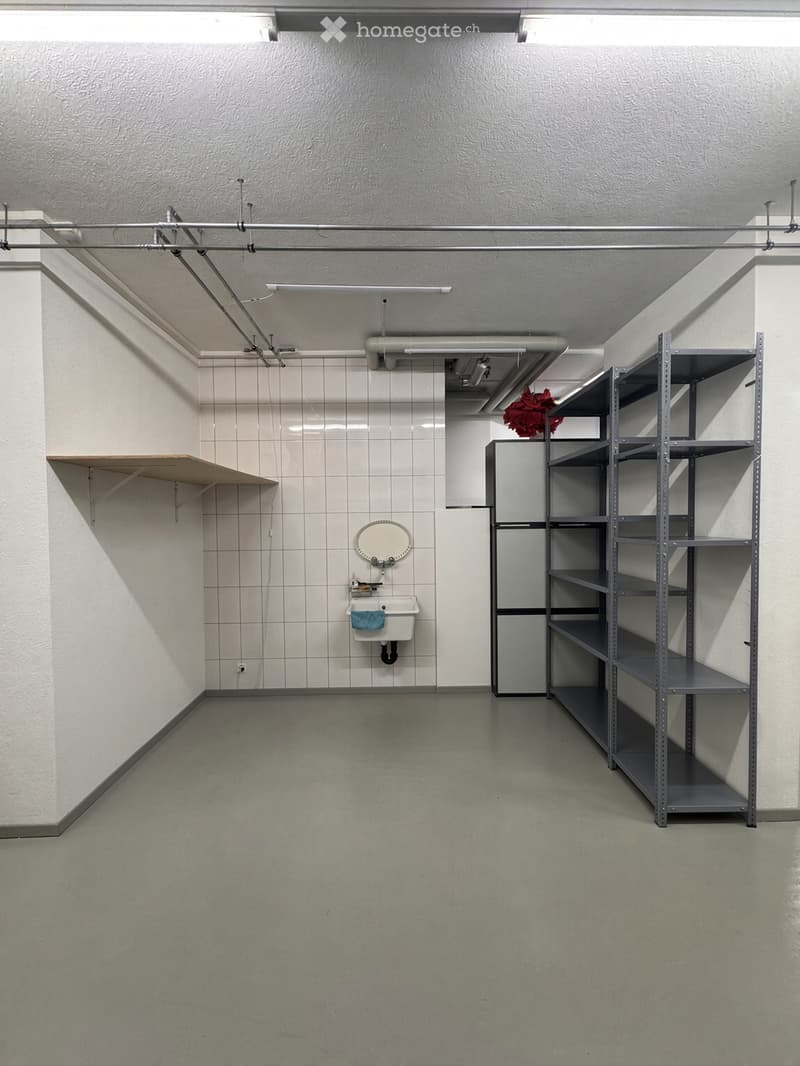 Minimalist bathroom with a white tiled wall, a single sink with a mirror above it, and a metal shelving unit on the right side.