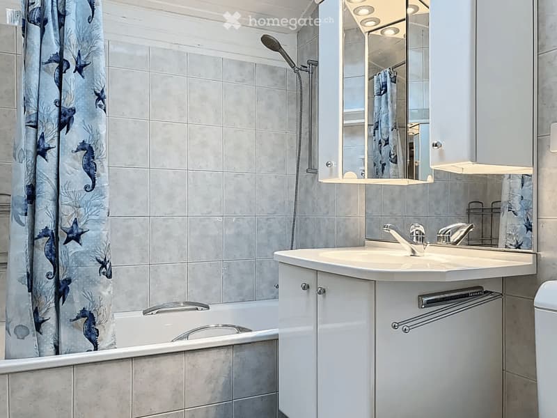Modern bathroom with a bathtub, sink, mirror, and shower area. Features a decorative shower curtain with sea creatures and a sleek, contemporary design.