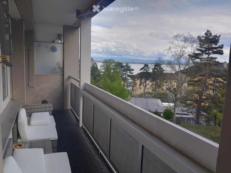 Balcony with a view of a lake and surrounding trees, featuring a white sofa and a small table.