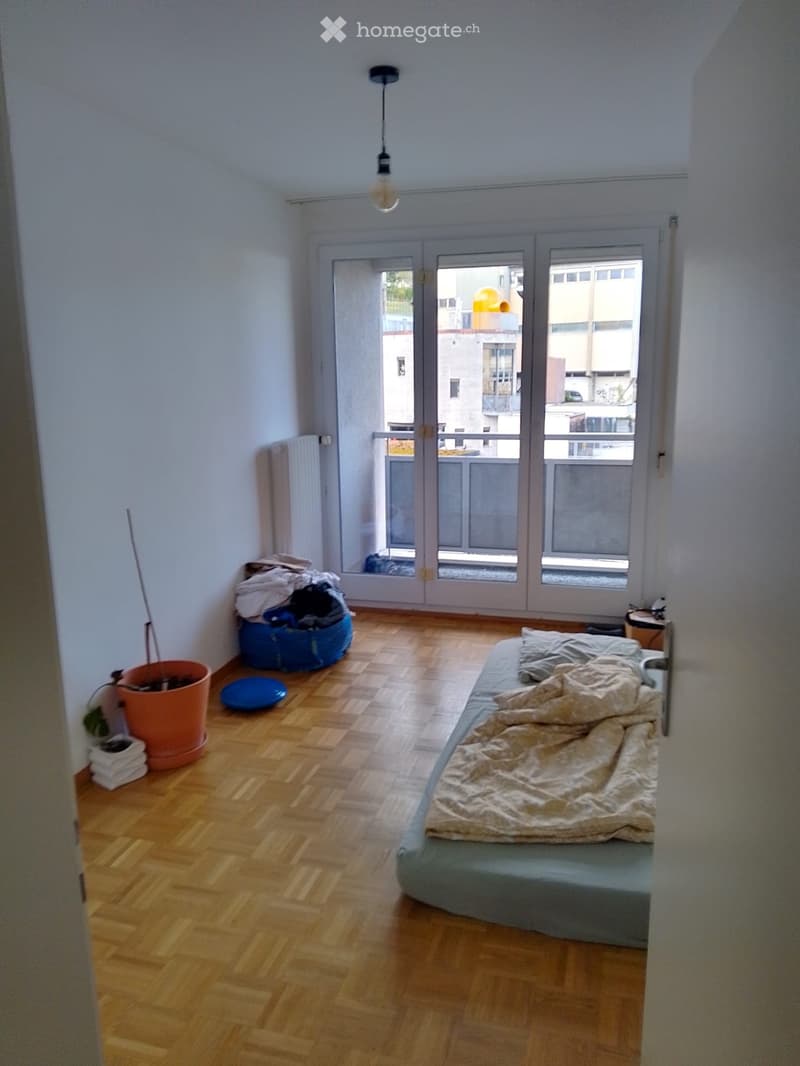 Bedroom with wooden flooring, a single bed with bedding, a radiator, a potted plant, and a storage bag near the window.
