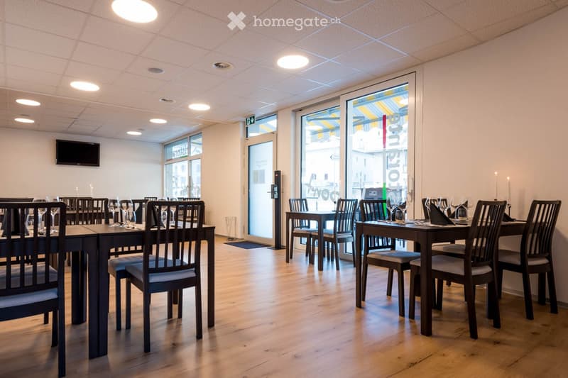 Restaurant or dining area with wooden tables, chairs, wine glasses, and a television mounted on the wall.