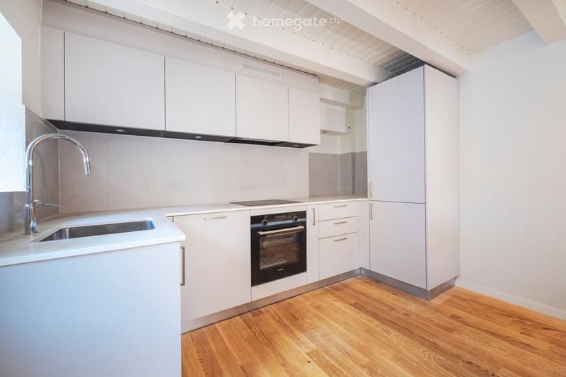 Modern kitchen with white cabinets, stainless steel sink and faucet, built-in oven, and wooden flooring.
