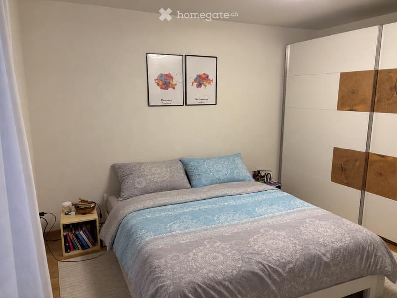 A modern bedroom with a double bed, nightstand, mirror wardrobe, and decorative picture frames on the wall.