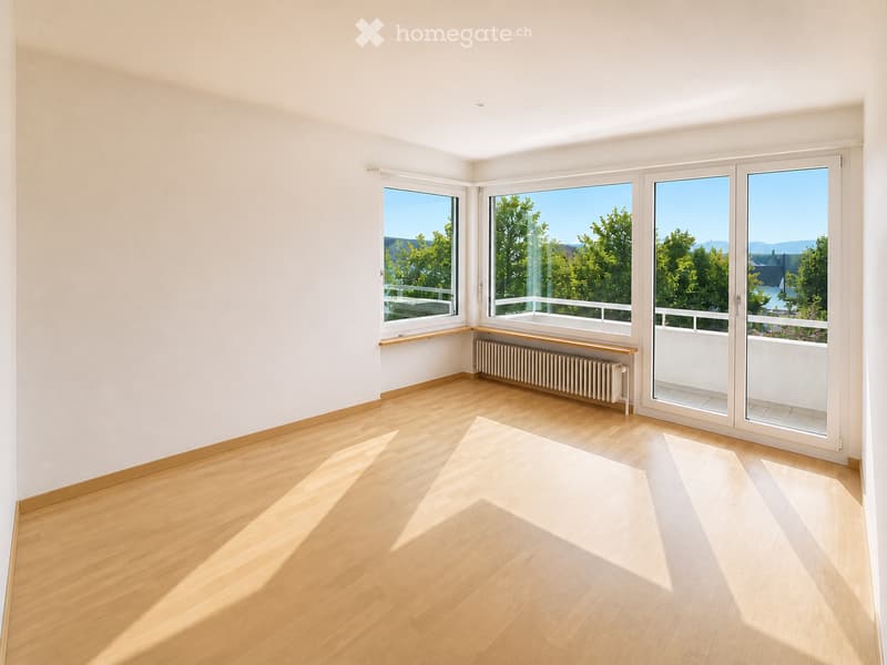 Empty room with wooden flooring, white walls, large windows, radiator, and a view of greenery and water.