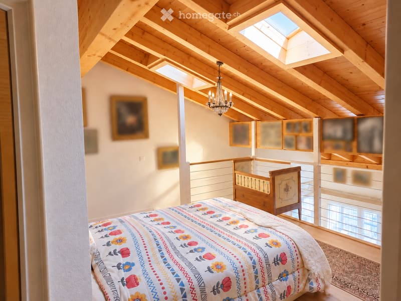 Cozy attic bedroom with wooden beams, skylight, chandelier, and colorful bedspread.