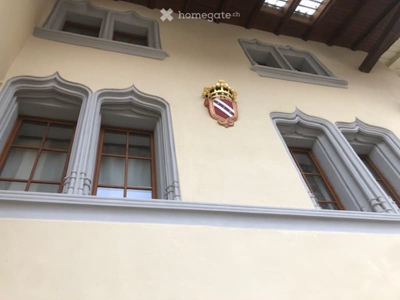 Facade with beige walls, three arched windows, and a coat of arms