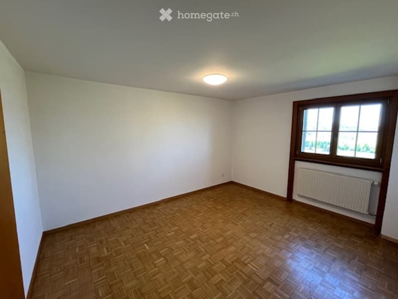 Empty room with wooden flooring, white walls, a single window with wooden frame, and a radiator below the window.
