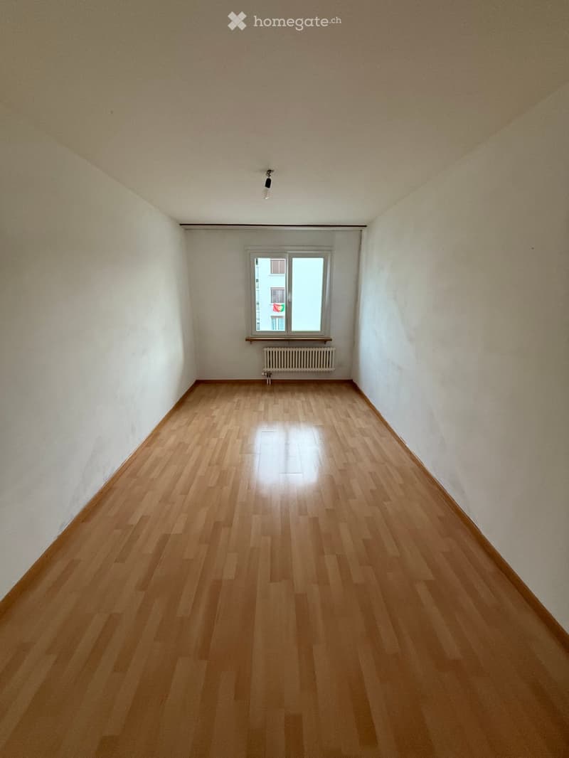 Empty room with wooden flooring, white walls, and a single window with a radiator below it.