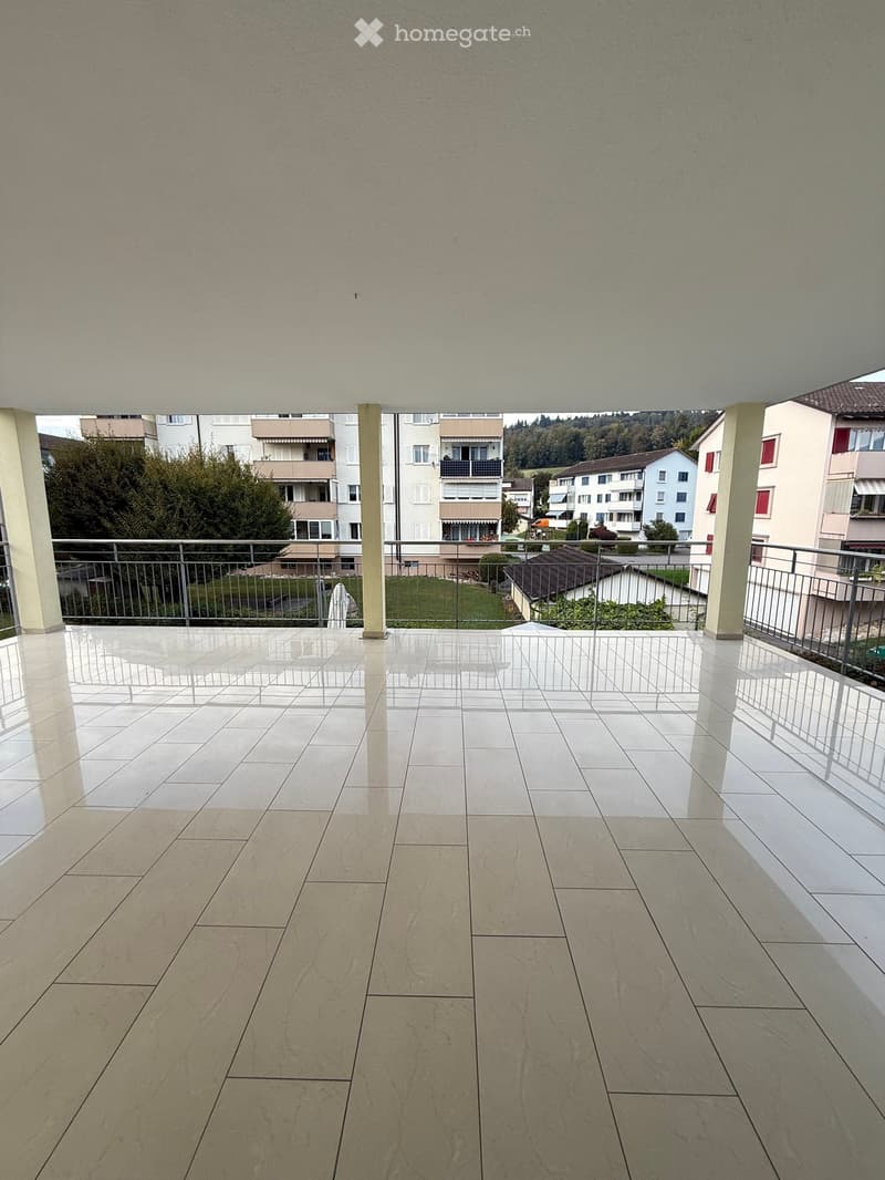 Balcony with tiled floor, metal railing, and view of surrounding buildings and greenery.