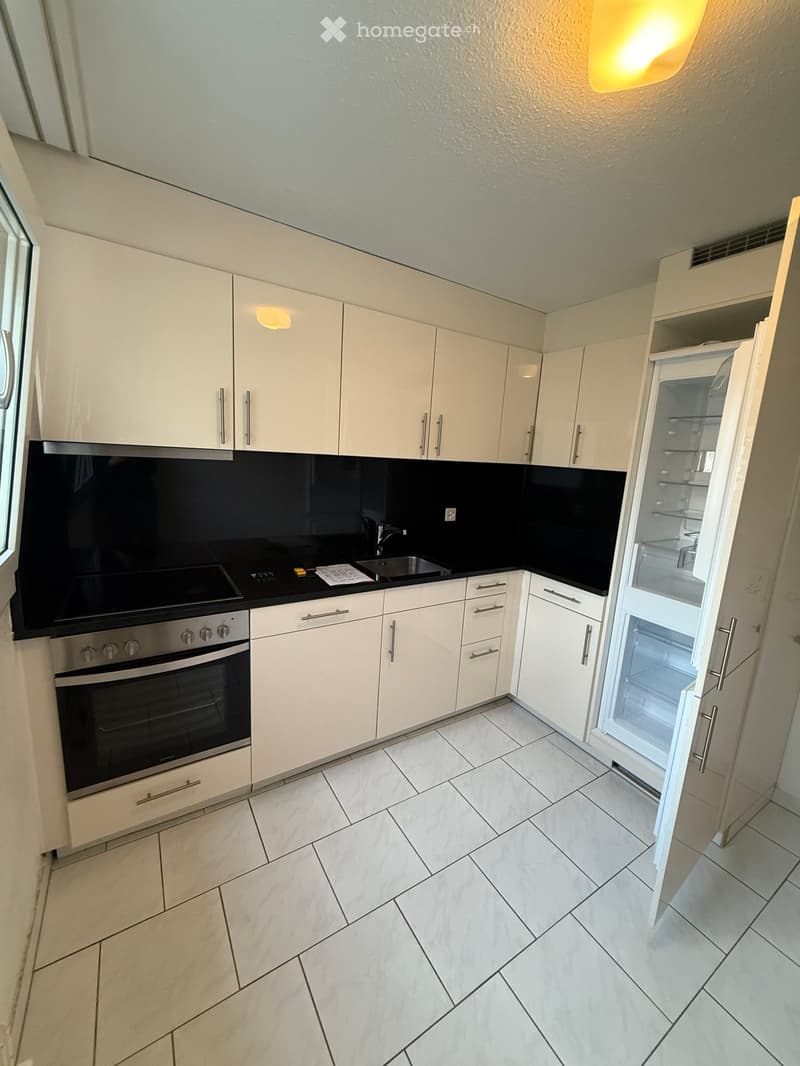 Modern kitchen with white cabinets, a stainless steel oven, a refrigerator, and a sink, featuring a black backsplash and tiled flooring.