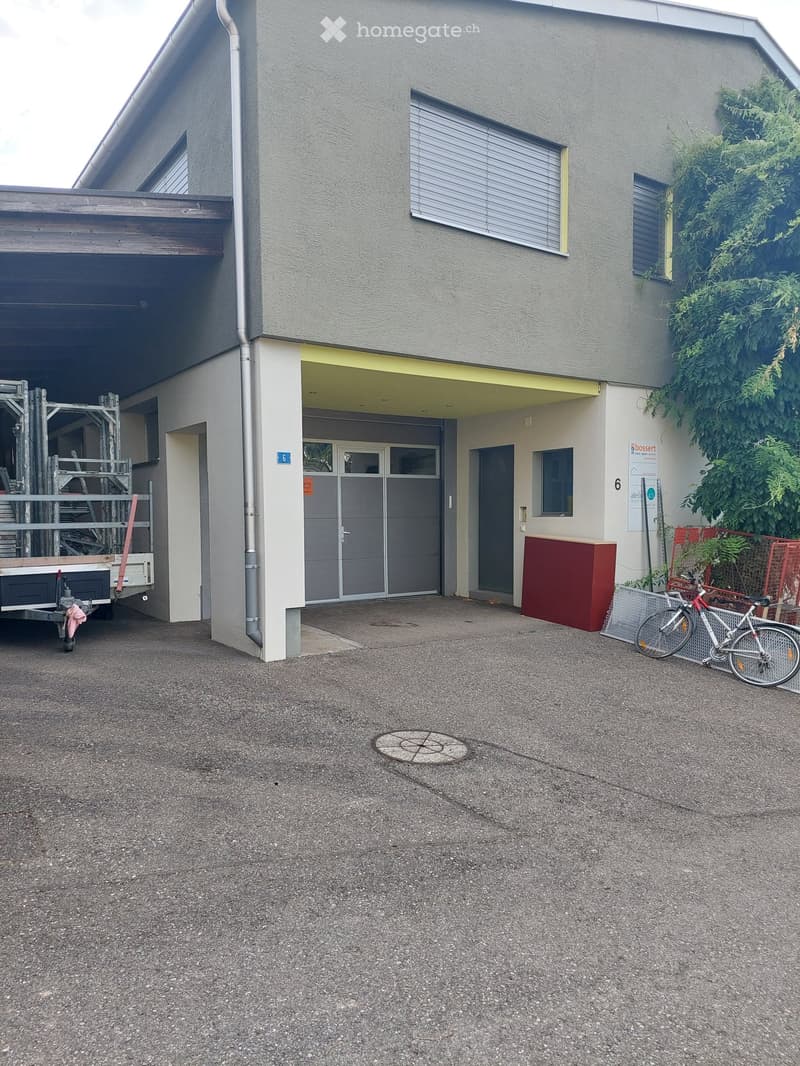 2-story house, gray exterior, windows with shutters, garage, bicycle parked in front, fenced area with plants