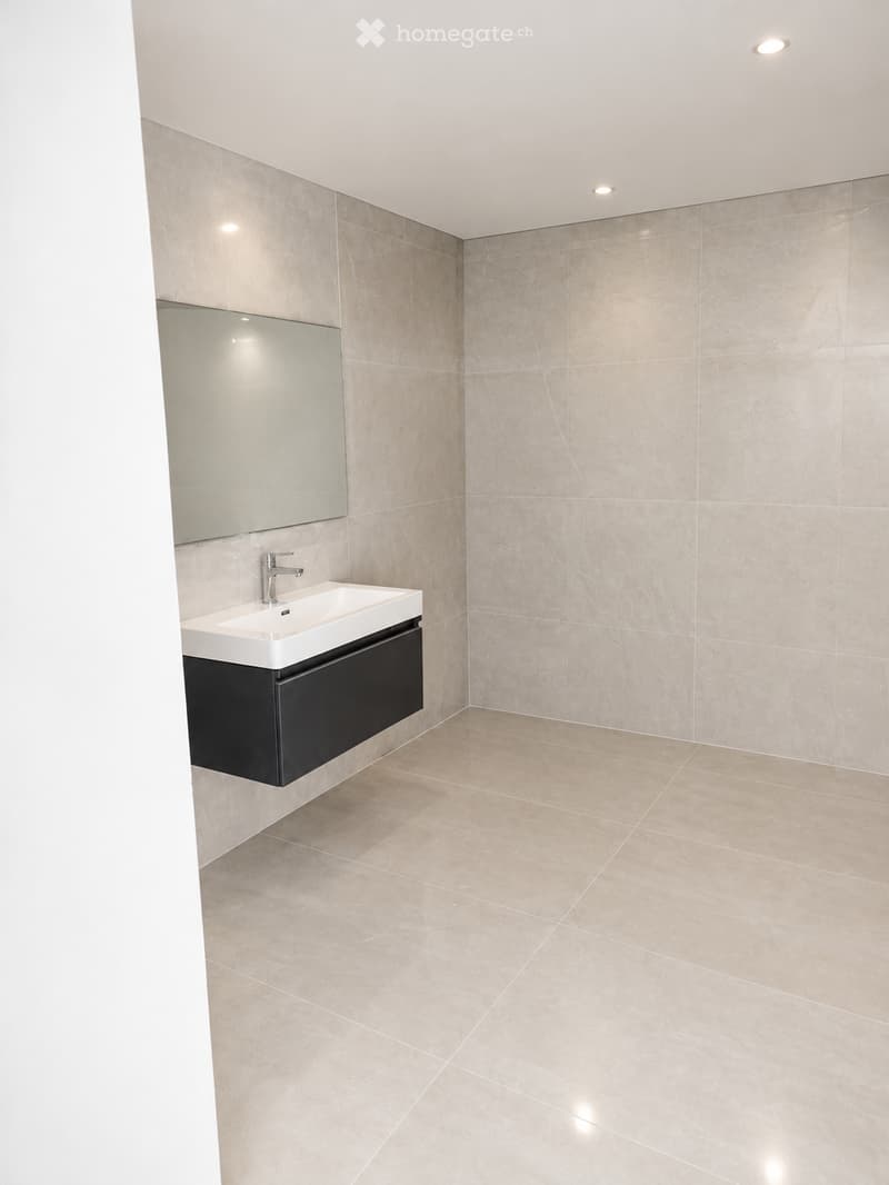 Modern bathroom with beige marble tiles, a white sink, a large mirror, and a black cabinet.