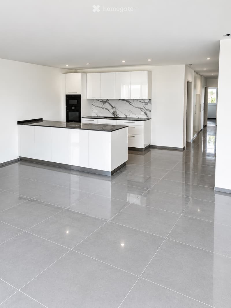 Modern kitchen with white cabinets, black countertop, and built-in oven. Features a central island with a black countertop and a marble backsplash.
