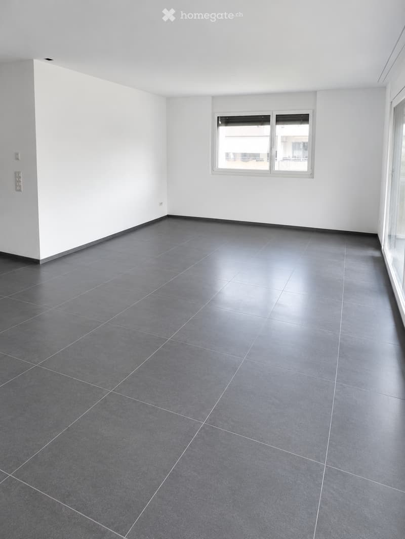 Empty room with grey tiled floor and white walls, featuring a large window and electrical outlets.