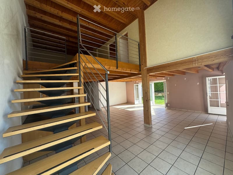 Spacious hallway with wooden staircase leading to an upper level, tiled floor, and large glass doors opening to an outdoor area.