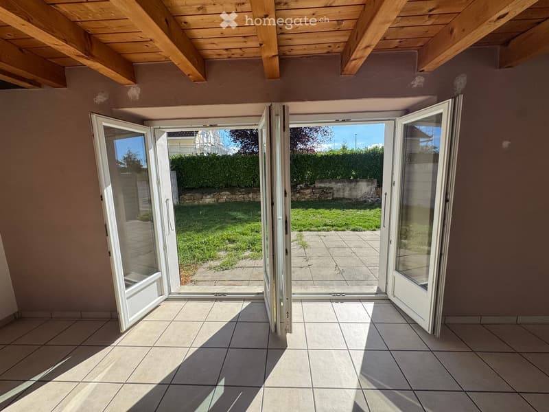 Empty room with tiled floor and large sliding glass doors leading to a garden area.