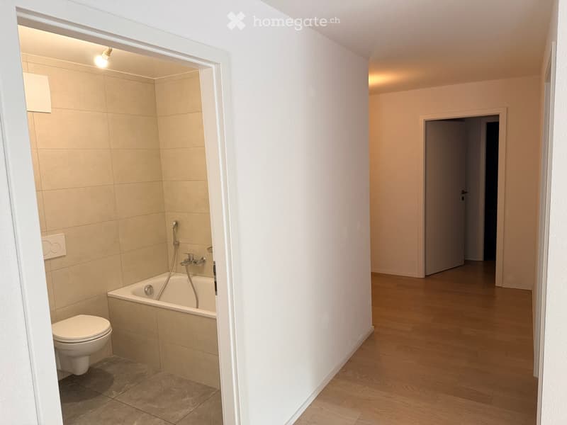 Modern bathroom with a toilet, bathtub, and a sleek faucet. The room features beige tiles and warm lighting.